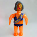 Orange glittery figurine with a purple sash and blue underwear on a white background
