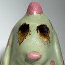 Ceramic dog like creature with green skin and pink polka dots on a neutral background