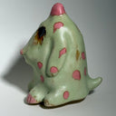 Ceramic dog like creature with green skin and pink polka dots on a neutral background
