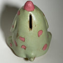 Ceramic dog like creature with green skin and pink polka dots on a neutral background