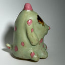 Ceramic dog like creature with green skin and pink polka dots on a neutral background