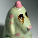 Ceramic dog like creature with green skin and pink polka dots on a neutral background