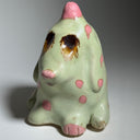 Ceramic dog like creature with green skin and pink polka dots on a neutral background