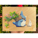 Painting on exposed wooden panel of a blue Chibi Totoro, holding a brown sack over its shoulder. Lush greenery and flowers burst from the bag behind.