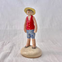 Ceramic sculpture of Luffy from One Piece, standing on a mound that looks like sand, with his iconic straw hat and his arms at his side.