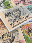 Memo pad with a sharp toothed cartoon cat on the cover, lunging forward. It is positioned atop a stack of similar notebooks with different colored covers but same illustration.