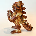 Ceramic sculpture of Garfield, entirely a muddy brown color. He is modeled like Godzilla with a large kaiju tail and holds a decapitated creature in his hand