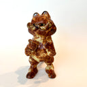 Ceramic sculpture of Garfield, entirely a muddy brown color. He is modeled like Godzilla with a large kaiju tail and holds a decapitated creature in his hand