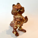 Ceramic sculpture of Garfield, entirely a muddy brown color. He is modeled like Godzilla with a large kaiju tail and holds a decapitated creature in his hand