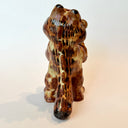 Ceramic sculpture of Garfield, entirely a muddy brown color. He is modeled like Godzilla with a large kaiju tail and holds a decapitated creature in his hand