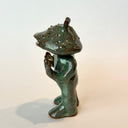 Ceramic sculpture of a catfish like creature, standing with a humanoid body. It has an open mouth and holds its hands slightly up.