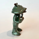 Ceramic sculpture of a catfish like creature, standing with a humanoid body. It has an open mouth and holds its hands slightly up.