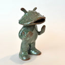 Ceramic sculpture of a catfish like creature, standing with a humanoid body. It has an open mouth and holds its hands slightly up.