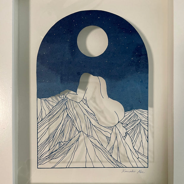  Delicate paper cutting made out of blue dyed paper of a woman's nude body sitting atop of a mountain range. She has no head and is turned away so only her back and butt are showing. A full moon is in the night sky.