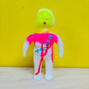 Colorful toy figure with a bright yellow head and pink and red torso against a yellow wall.