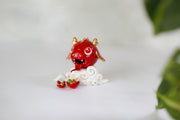 Glazed ceramic sculpture of a cute red dragon head with gold color accents. It's propped up on a cloud and in front are 2 bowls, one with food and the other with gold tokens.