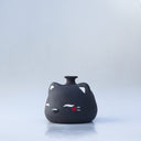 Small, short black jar with a painted on cat face, with closed eyes and red cheeks. It has a small spout opening.