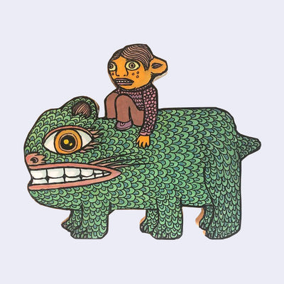 Die cut wooden sculpture of a small boy riding atop of a green monster with a large mouth and 6 legs.