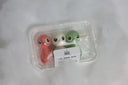 Sculpture of small characters shaped and colored to look like dango, with a stick going through their heads. They have cute eyes and a simple nose as their only facial feature. They are in product packaging, like they are being sold in a convenience store.