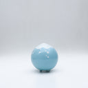 Small glossy blue ceramic sculpture of a round character with tiny legs and a closed eye peaceful expression. The top of its head is white like a snow capped mountain.