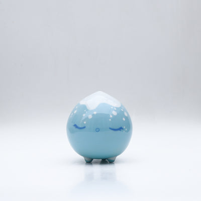 Small glossy blue ceramic sculpture of a round character with tiny legs and a closed eye peaceful expression. The top of its head is white like a snow capped mountain.