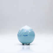 Small glossy blue ceramic sculpture of a round character with tiny legs and a closed eye peaceful expression. The top of its head is white like a snow capped mountain.