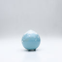Small glossy blue ceramic sculpture of a round character with tiny legs and a closed eye peaceful expression. The top of its head is white like a snow capped mountain.