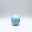 Small glossy blue ceramic sculpture of a round character with tiny legs and a closed eye slightly angry expression. The top of its head is white like a snow capped mountain.