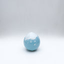 Small glossy blue ceramic sculpture of a round character with tiny legs and a closed eye slightly angry expression. The top of its head is white like a snow capped mountain.