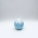 Small glossy blue ceramic sculpture of a round character with tiny legs and a closed eye slightly angry expression. The top of its head is white like a snow capped mountain.