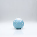 Small glossy blue ceramic sculpture of a round character with tiny legs and a closed eye gleeful expression. The top of its head is white like a snow capped mountain.