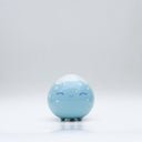Small glossy blue ceramic sculpture of a round character with tiny legs and a closed eye gleeful expression. The top of its head is white like a snow capped mountain.
