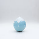 Small glossy blue ceramic sculpture of a round character with tiny legs and a closed eye, slightly pouty expression. The top of its head is white like a snow capped mountain.