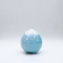 Small glossy blue ceramic sculpture of a round character with tiny legs and a closed eye, sleepy expression. The top of its head is white like a snow capped mountain.