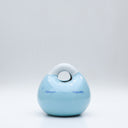 Ceramic sculpture made to look like a smooth handbag, blue with a cute cartoon face on it. It has a closed eye expression with a small smile and white dots along the top, like a snowcapped mountain.