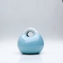 Ceramic sculpture made to look like a smooth handbag, blue with a cute cartoon face on it. It has a closed eye expression with a small smile and white dots along the top, like a snowcapped mountain.
