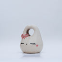 Ceramic sculpture made to look like a purse, with a cute closed eye bunny face and rosy cheeks. It has a pink bow atop its head.