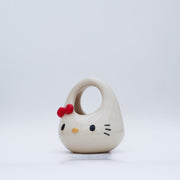 Ceramic sculpture made to look like a purse, with the face of Hello Kitty, with her iconic red bow in the upper right side of her head.