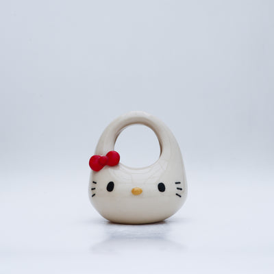Ceramic sculpture made to look like a purse, with the face of Hello Kitty, with her iconic red bow in the upper right side of her head.