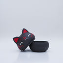 Black clay pot with a lid that looks like a fox's head, a matching black color with red ears and face paint. It has closed eyes and a small white nose. The bowl has no body details.