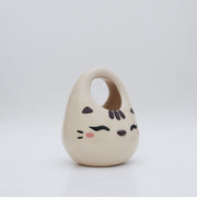 Ceramic sculpture made to look like a purse, with the face of a cute, closed eye cat with rosy cheeks and 3 stripes at the top of its head.