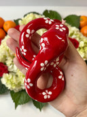Ceramic sculpture of a red snake with large, cute eyes and white flower patterning atop its body. It has its tongue out and is seen from overhead.