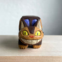 Whittled wooden sculpture of a cat shaped like a bus from My Neighbor Totoro. Its tail sticks straight out and it has a smiling face.