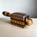 Whittled wooden sculpture of a cat shaped like a bus from My Neighbor Totoro. Its tail sticks straight out and it has a smiling face.