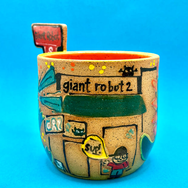 Ceramic mug with brightly painted graphics and a slab that juts out, that reads "Giant Robot Store." Drawings show a small person with glasses in front of GR2 Gallery.