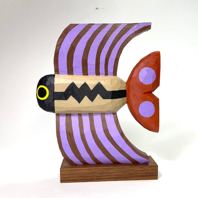 Painted whittled wooden sculpture of a fish with tall fins, striped brown and purple. The body is tan with a Charlie Brown esque stripe.