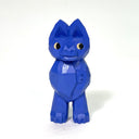 Blue whittled wood sculpture of a bat, with pointed ears, a snout and eyes looking off to the side. It stands on legs with its wings wrapped around itself, like a shawl.