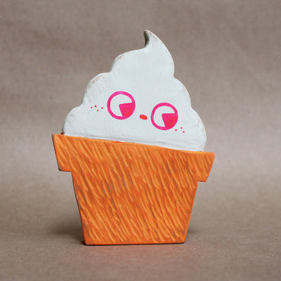 Painted die cut wooden sculpture of a cone of soft serve ice cream, white with a simple pink face drawn on. 