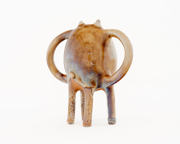 Ceramic sculpture of a brown character with small ears and eyes and standing on four thin legs. It has mug handle like shapes coming out of its sides.