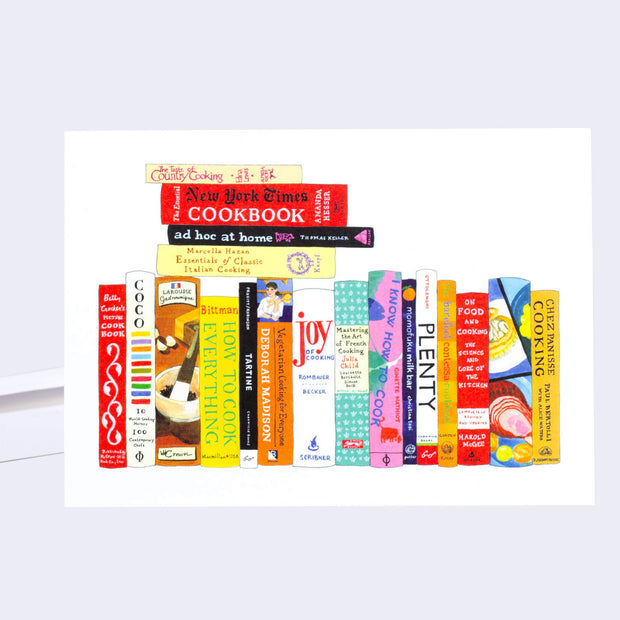 White greeting card with an illustration of lined up books and some piled on top, featuring many well known cookbooks such as: Joy of Cooking, The Taste of Country Cooking, etc.